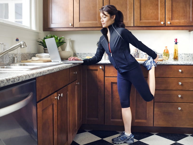 busy woman works on laptop in kitchen while exercising