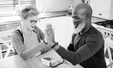 Black man and white woman at home at kitchen table checking blood pressure
