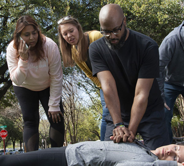 bystander performing CPR on an unresponsive person, another bystander is calling 911