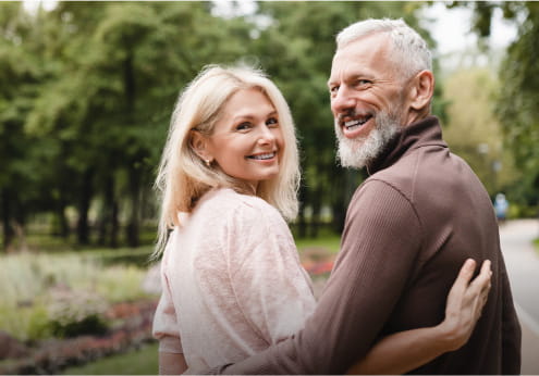 Couple walking together out doors, looking back over their shoulder at camera