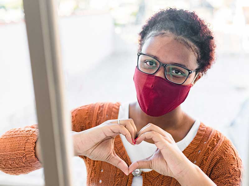 woman wearing mask motioning heart with hands