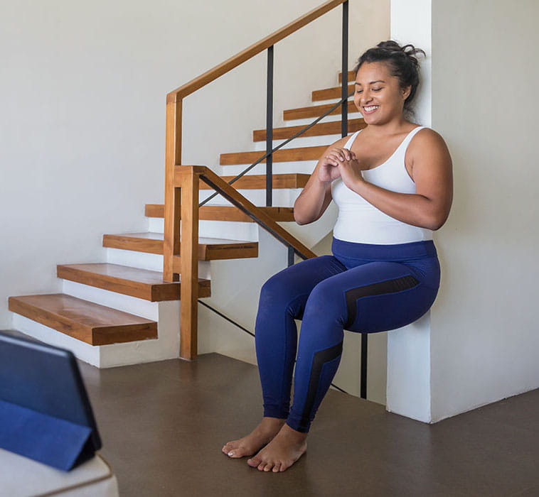 Woman practicing squats against a wall at home