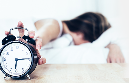 Girl in bed out of focus reaching to turn off alarm clock