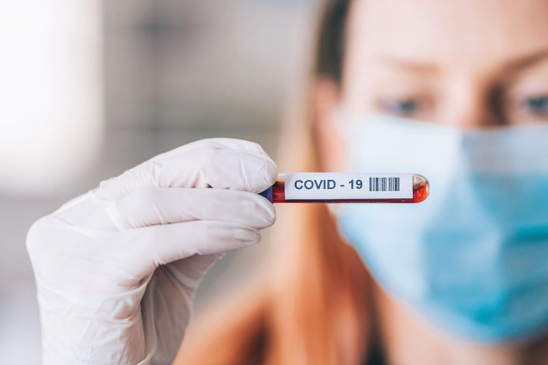 Woman technician wearing mask holding vial marked COVID-19