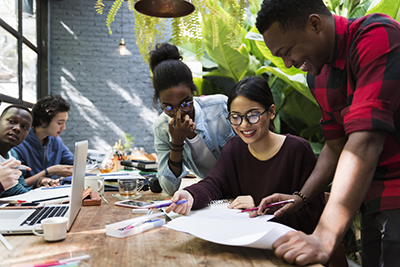 group of diverse young adults gathered around a table working together on a project and smiling 