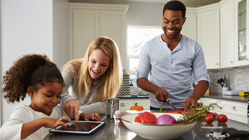 Diverse family eating in kitchen and using tablet