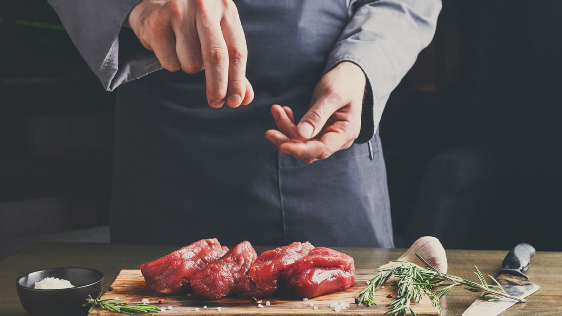man's hands adding salt to meat while cooking