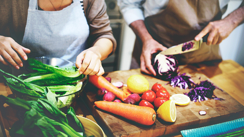 Pareja picando verduras en la tabla de cortar