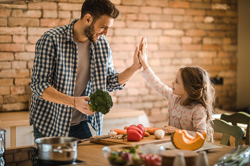 father holding broccoli high-five daughter