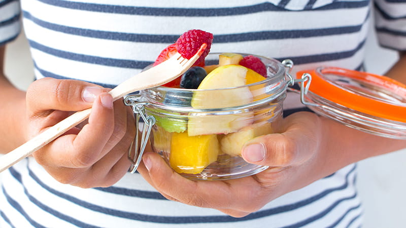 close up of hands eating fruit in a mason jar with fork