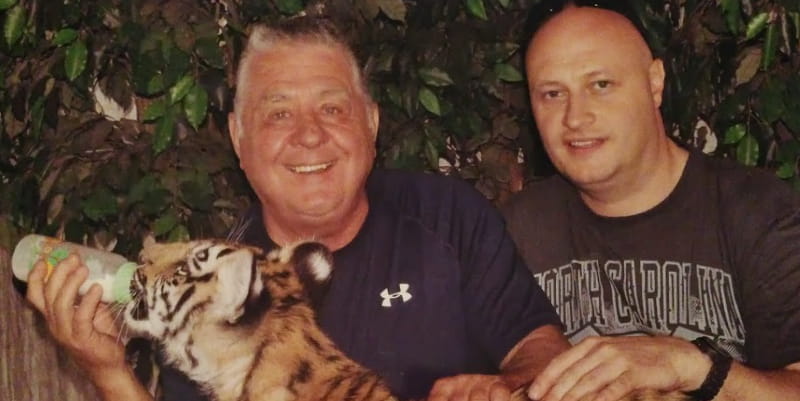Heart valve disease survivor Len Rapkins (left) bottle-feeds a tiger cub with son Marc Faux (right).