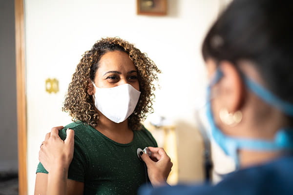 Doctor listening to patient's heart wearing protective face masks