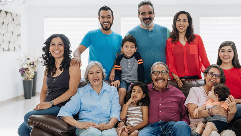A multigenerational Hispanic family sitting around a sofa and posing for the camera