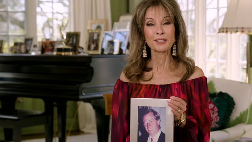a video frame of Susan Lucci in a living room holding a framed photo of her husband