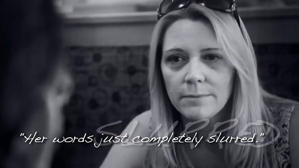 A black and white video screen shot of stroke survivor, Julie, a white woman talking with a friend indoors with the overlaying words, "Her words just completely slurred."