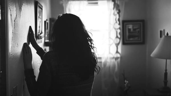 Una fotografía en blanco y negro de una mujer sujetándose de la pared de una sala