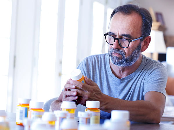 An older Latino man is sitting at a table sorting through prescription medications.