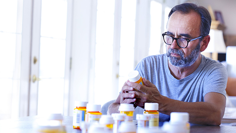 An older Latino man is sitting at a table sorting through prescription medications.