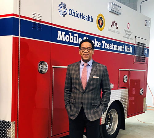 Dr. William Hicks is smiling while standing next to a Mobile Stroke Treatment Unit ambulance