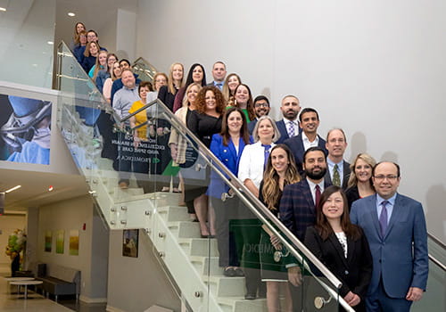 a group photo of ProMedica Stroke Network staff smiling and standing on a staircase in a business office setting