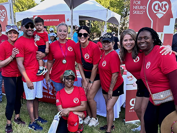 A group photo of Centre for Neuro Skills representatives are posing in front of their booth at an outdoor event.