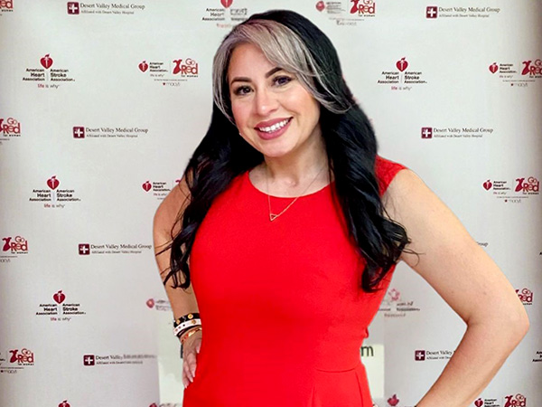 Brisa Alfaro posa con un vestido rojo frente a un fondo de pasos y repeticiones Go Red For Women de la Asociación Estadounidense del Corazón.