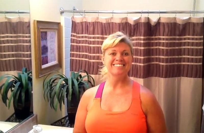 A smiling White woman wearing workout clothing is standing in a bathroom.