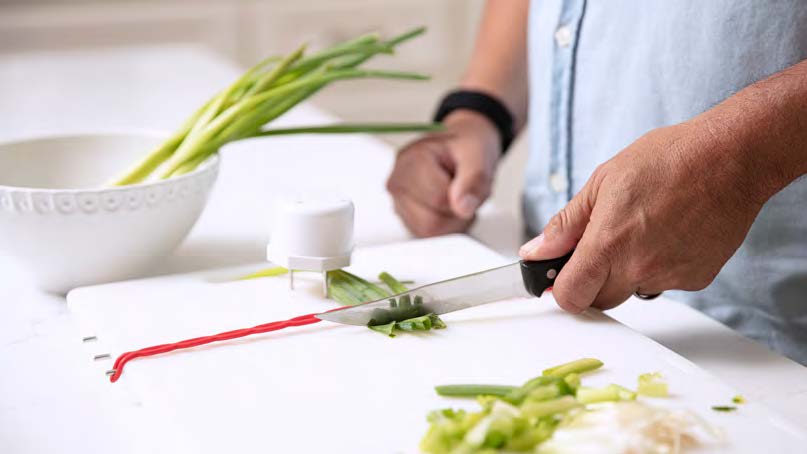 A close-up view of a hand chopping vegetables with a knife.