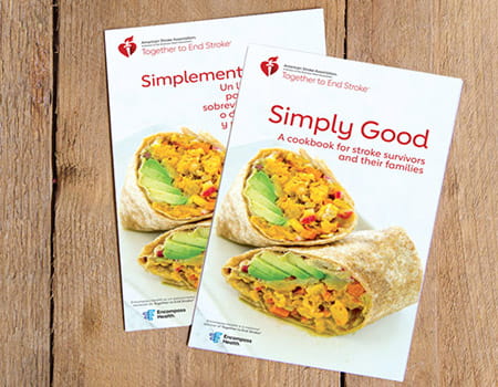 The Simply Good Cookbook and Simplemente Bueno un Libro de Recetas are laying overlapped on wood planks.
