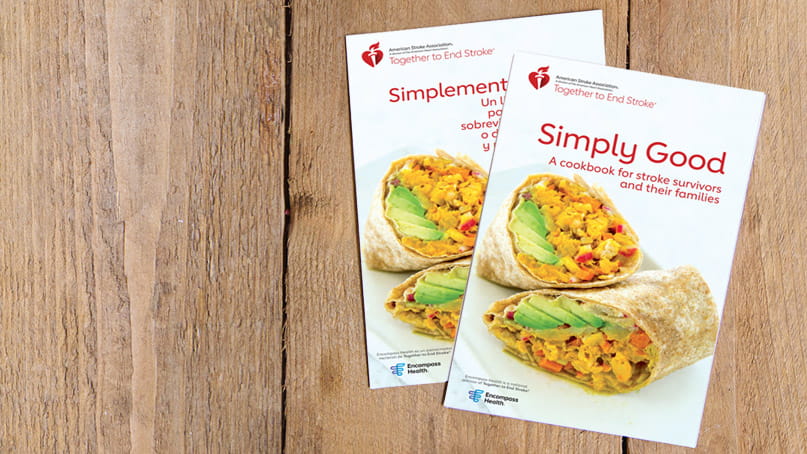 The Simply Good Cookbook and Simplemente Bueno un Libro de Recetas are laying overlapped on wood planks.