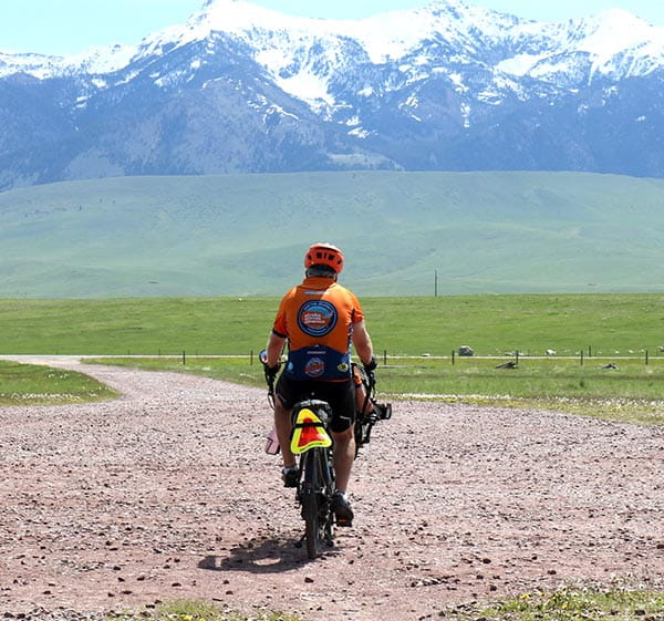 Man on a motorcycle driving toward snow-capped mountains