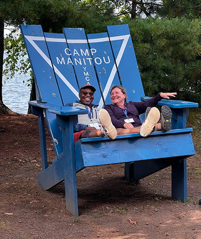 two people sitting in a giant blue Adirondack chair in an outdoor setting