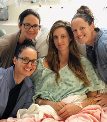 Stroke survivor, Kaitlyn Fieseler, is sitting in a hospital bed surrounded by her sisters