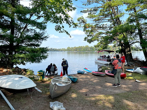 a group of people in life jackets at the lake preparing to canoe and boat