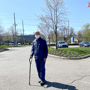 Mukul Pandya is masked and standing with the help of a cane in a parking lot on a clear day.