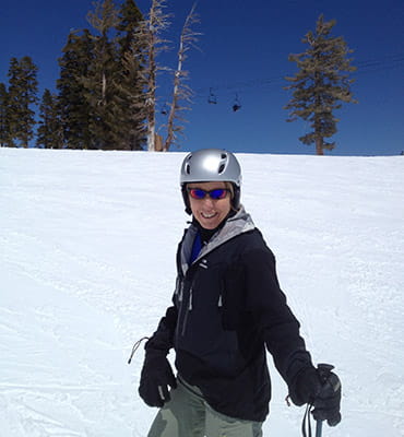 Deb Meyerson is wearing ski gear and posing on a ski slope.