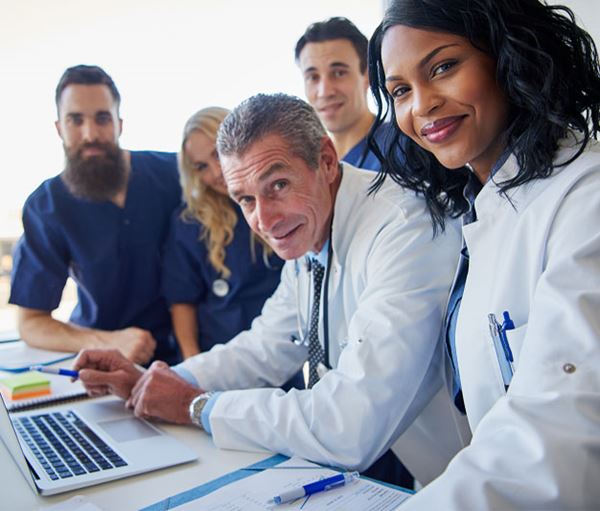 A diverse group of medical professionals are posing around a laptop and smiling. Group of doctors standing together