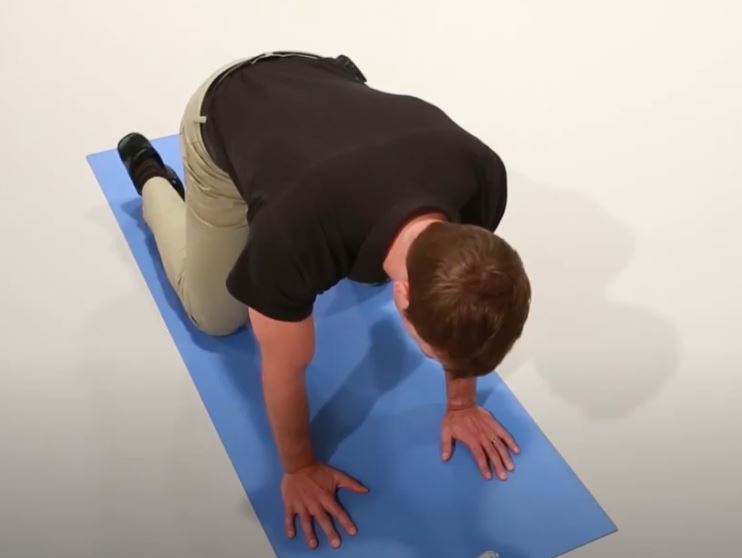 A White man is on his hands and knees on a yoga mat.