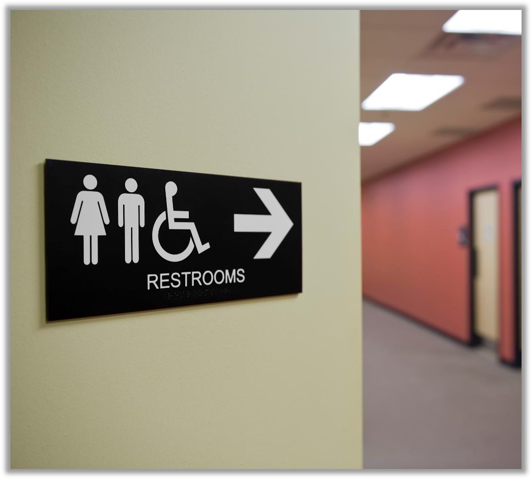 office hallway with a sign showing female, male, and wheelchair icons, and an arrow pointing to the restrooms