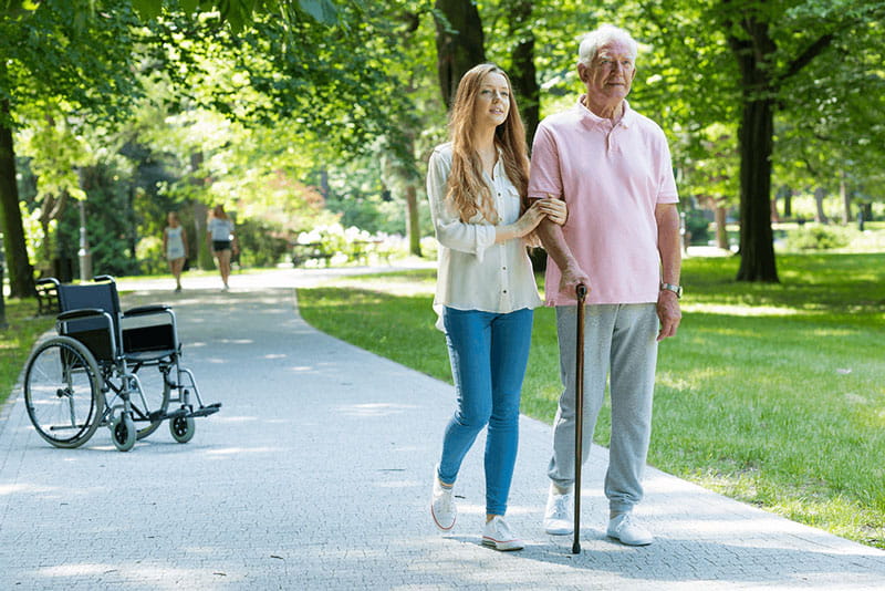 woman helping elderly father with cane