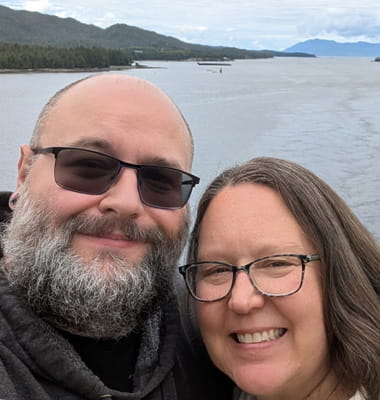 A selfie of stroke survivor Chris Rose and his wife with a body of water and mountains in the background