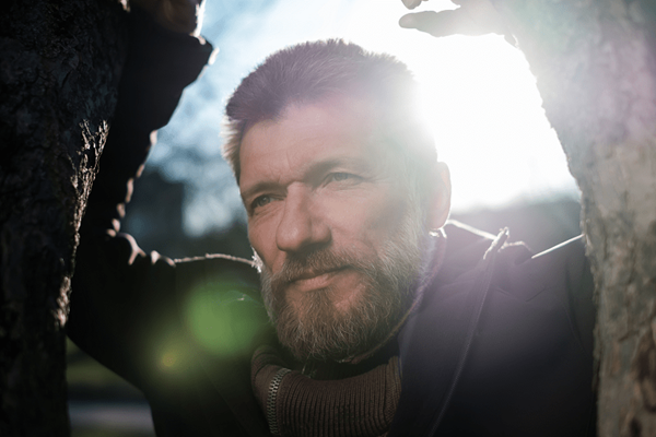 Older man standing in a park leaning against a tree