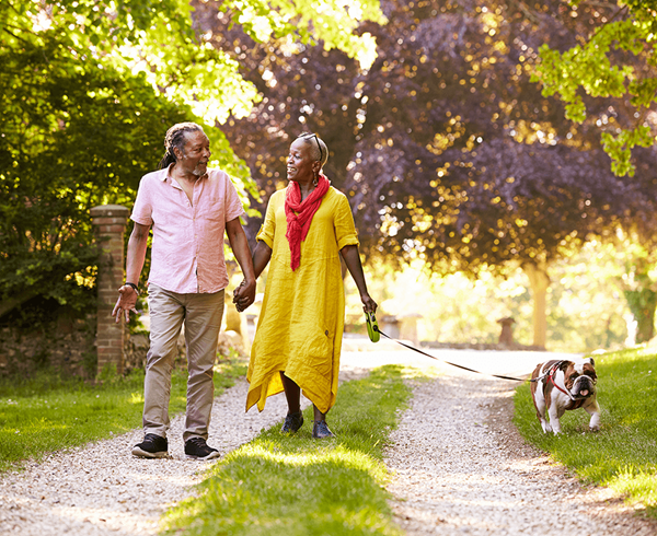 Senior couple walking with pet bulldog down grassy lane