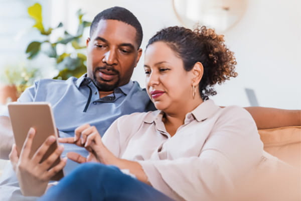 A man and woman sitting on a sofa are interacting with a touchscreen device. A man and woman sitting on a sofa are interacting with a touchscreen device.