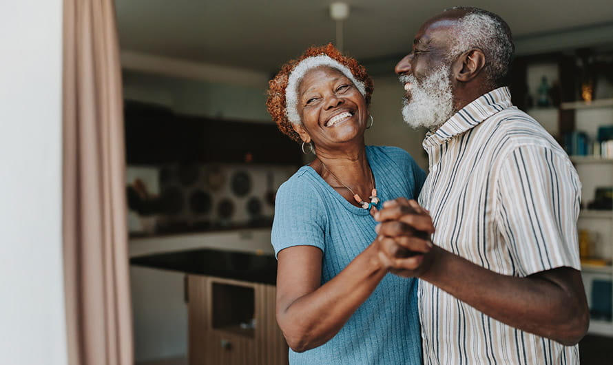An older man and woman are smiling and dancing in a kitchen. An older man and woman are smiling and dancing in a kitchen.