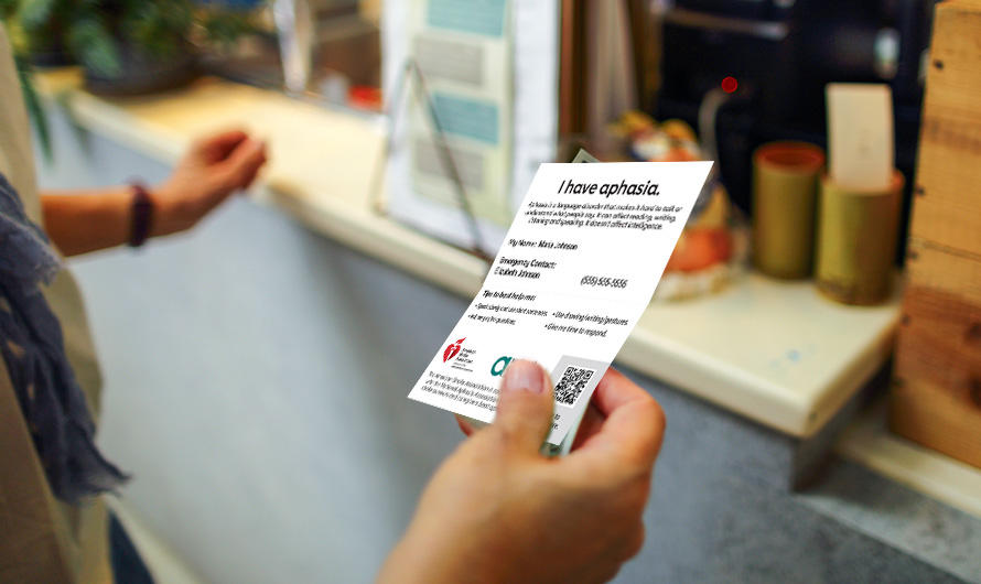 A person is holding their aphasia ID card in their hand to show at a retail counter. A person is holding their aphasia ID card in their hand to show at a retail counter.