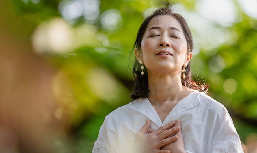 A woman is closing her eyes, doing a breathing exercise and meditating in nature. A woman is closing her eyes, doing a breathing exercise and meditating in nature.