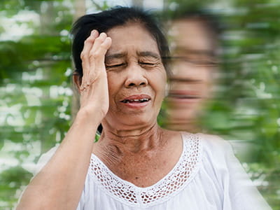 An older woman is holding her head while her surroundings are blurred.