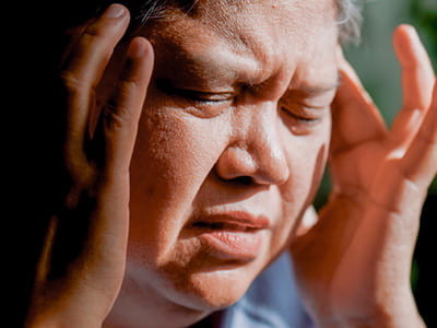 A person is holding the sides of their head with their eyes tightly closed.