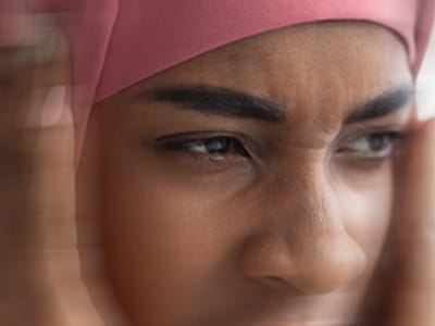 A blurred Somali woman is squinting her eyes and holding her head